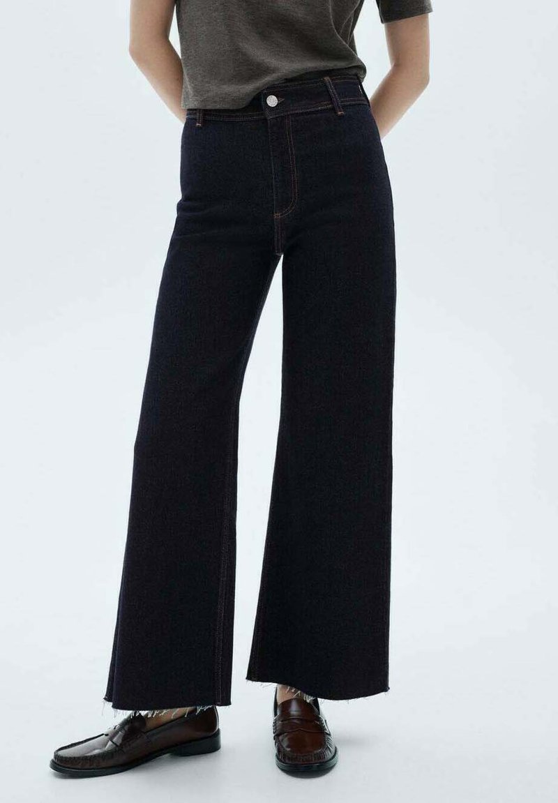 Wijduitlopende jeans van donkerdenim, met een hoge taille, raw hem en contrasterende stiksels. Gecombineerd met bruine leren instappers.