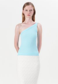 Lyseblå, ribbet tanktop med en skulderstrop, parret med en struktureret hvid nederdel. Toppen har et tætsiddende design.