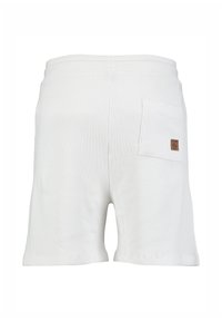 Shorts blancs texturés avec une ceinture élastique et une poche arrière arborant une petite étiquette en cuir marron sur le côté droit.