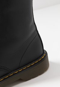 Bottines en cuir noir avec une finition lisse, des coutures jaunes contrastantes et une semelle intérieure en caoutchouc brun striée. Bout arrondi distinctif et design robuste.