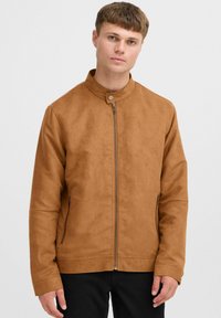 Veste marron en imitation daim avec col montant, fermeture éclair à l'avant et poches latérales. Présente une texture lisse et un design minimaliste.