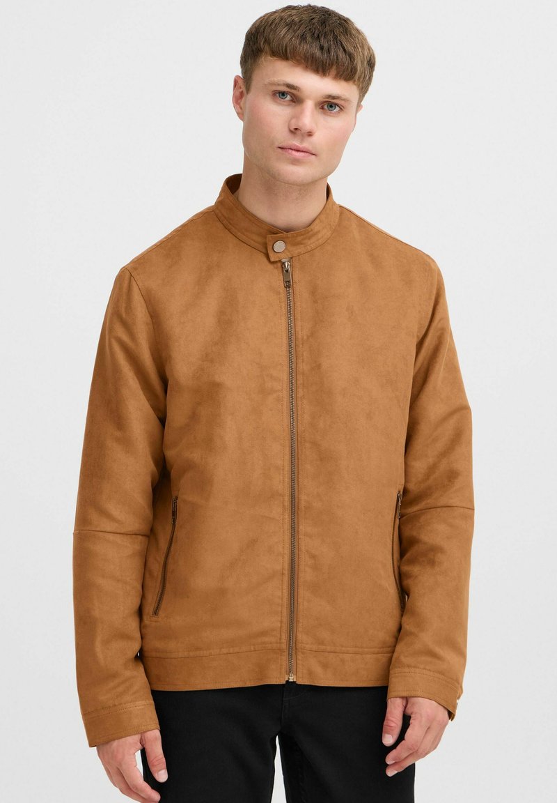 Veste marron en imitation daim avec col montant, fermeture éclair à l'avant et poches latérales. Présente une texture lisse et un design minimaliste.