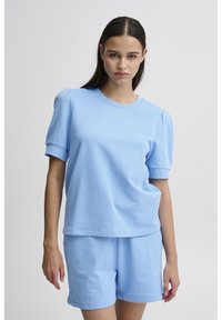 Set in cotone azzurro chiaro composto da una maglietta a maniche corte con maniche a sbuffo e pantaloni corti coordinati, entrambi in una consistenza morbida e liscia.