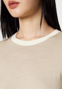 Pull en maille beige avec un col rond côtelé crème. Présente une texture lisse et une silhouette ajustée.