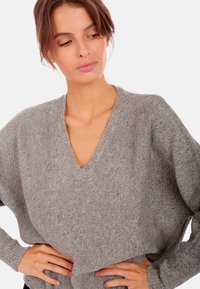 Pull en tricot gris à col en V avec une coupe décontractée et un tissu texturé. Poignets et ourlet côtelés, mettant en avant un design moderne et décontracté.
