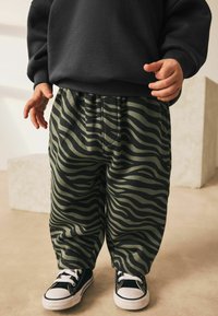 Green and black striped sweatpants with a relaxed fit, paired with black and white sneakers, featuring a comfortable elastic waistband.