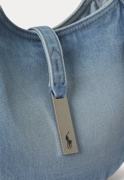 Világoskék farmer táska varrott fogantyúval és téglalap alakú, ezüst színű fémtábla, amelyen egy pólójátékos logó látható.