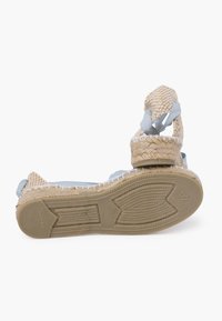 Espadrilė stiliaus sandalai su aštuonių dalykų viršumi, šviesiai mėlynomis juostelėmis, plokščiu padu ir tekstūruotu guminio pado paviršiumi. Savybės apima audinį dizainą ir ankle kaklaraiščius.