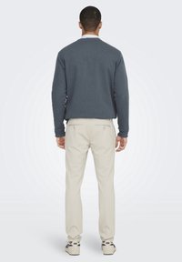 Felpa blu scuro con maniche lunghe, pantaloni chinos beige e sneakers. L'outfit è casual con linee semplici e senza motivi visibili.