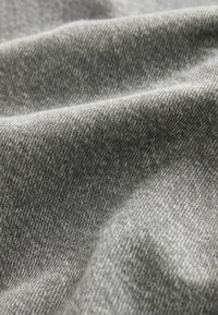 Gros plan sur un tissu gris texturé et plié, montrant un motif de tissage fin en diagonale et des contours doux et drapés.