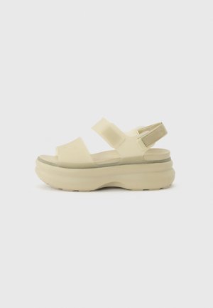 Sandale plateforme beige avec deux larges brides sur le pied et une bride ajustable avec fermeture Velcro à la cheville.