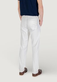 Pantaloni bianchi in cotone con vestibilità dritta, dotati di tasche posteriori. Indossati con una maglia blu navy e scarpe marroni, a sottolineare un design casual.