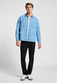 Ljusblå denimskjorta med två framfickor, knapplist och avslappnad passform, ihopparad med svarta byxor och vita sneakers.