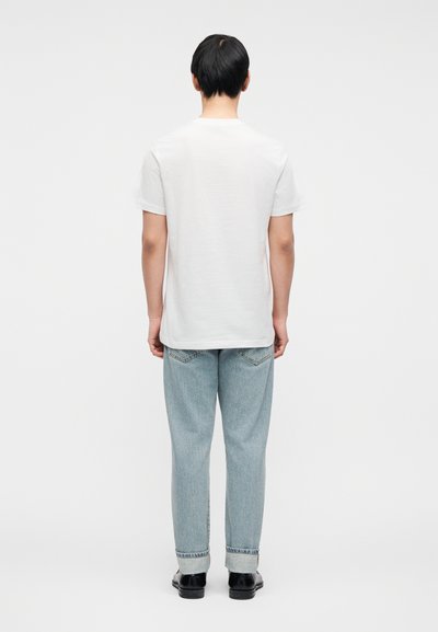 Άσπρο βαμβακερό T-shirt με κοντά μανίκια, συνδυασμένο με ανοιχτό μπλε τζιν παντελόνι. Το παντελόνι έχει ίσια γραμμή και γυρισμένα μπατζάκια.