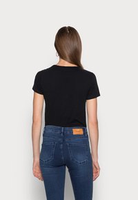 Camisa negra de manga corta combinada con unos pantalones ajustados azul oscuro que cuentan con un parche de cuero en la parte trasera de la cinturilla y bolsillos estándar.