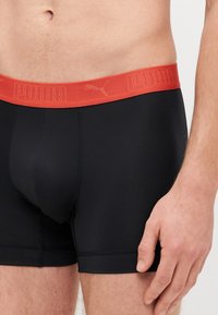 Black boxer briefs with a red elastic waistband featuring embossed "PUMA" logo. Smooth fabric and form-fitting design, short leg length.