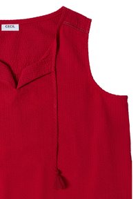 Haut rouge sans manches texturé avec un col en V, un lien décoratif à pompons et une étiquette de marque à l'intérieur du col.