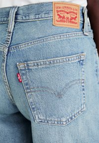 Ljusblå Levi's denimjeans i närbild som visar bakfickan, den röda Levi's-taggen och den bruna läderlogotypen på midjebandet.