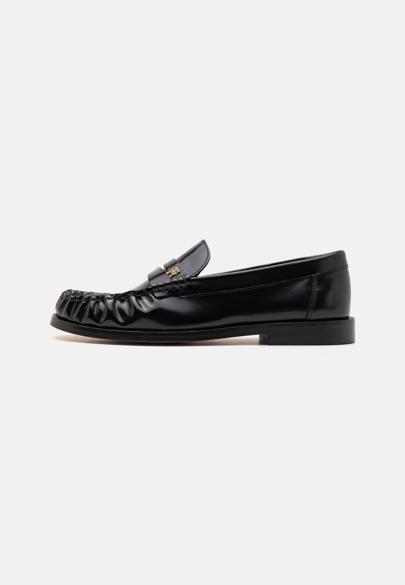 Mocassin en cuir noir avec un bout arrondi, texture plissée à l'avant et semelle plate. Présente un petit accent métallique sur la lanière.