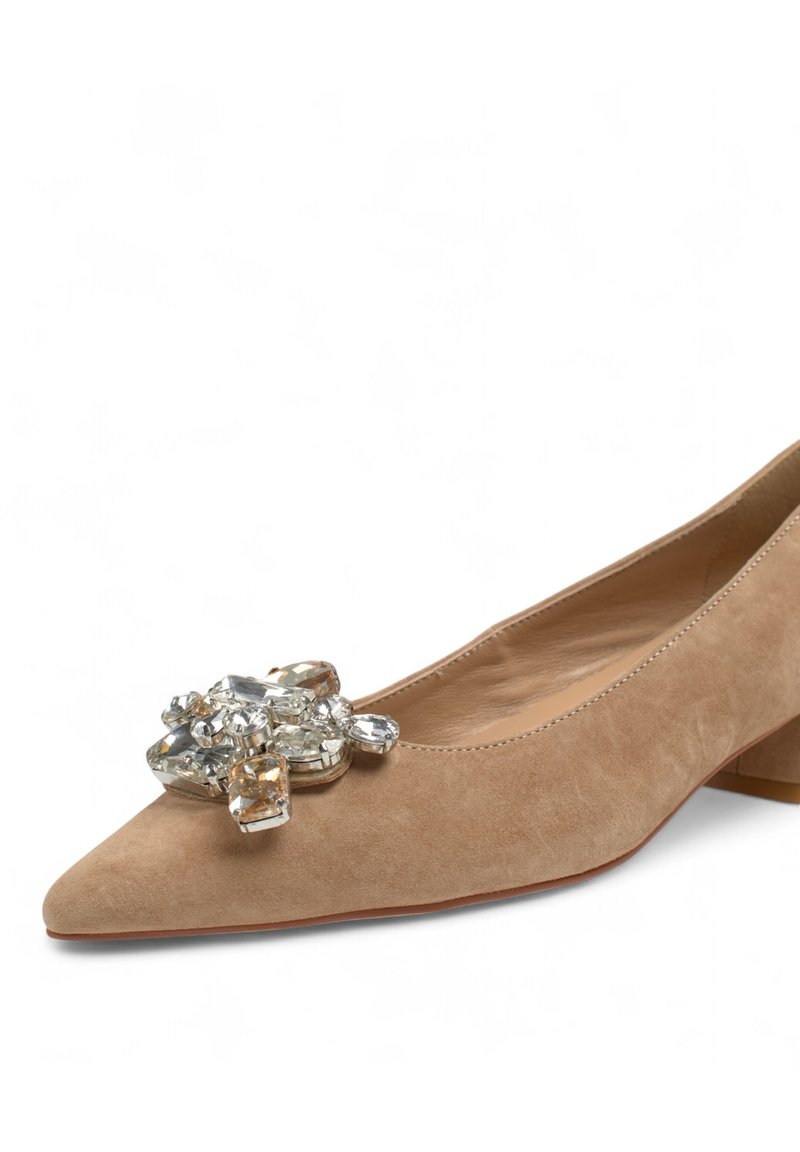 Scarpa bassa in suede beige con tacco basso e punta affusolata, caratterizzata da un ornamento decorativo in gemme trasparenti sul davanti e una morbida fodera interna.
