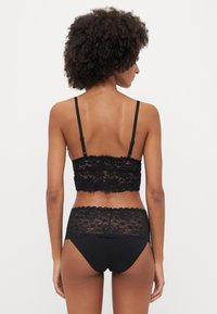 Must mustriba mustra, mis samet ja lillemustriga detailidega. Mustad pitsist bralette, millel on reguleeritavad rihmad, koos sobivate mustade pitsist tagajalgadega aluspükstega. Lainelised servad ja lilleline muster kogu ulatuses.