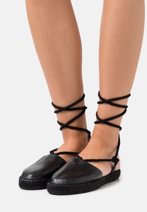 Chaussures espadrilles noires avec lanières à nouer autour de la cheville, fabriquées en cuir à finition texturée et semelle en jute tressée.