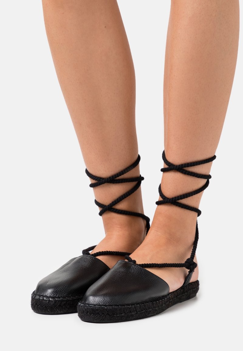 Chaussures espadrilles noires avec lanières à nouer autour de la cheville, fabriquées en cuir à finition texturée et semelle en jute tressée.