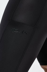 Zwarte sportleggingen met een soepel textuur, ademend mesh-paneel en reliëf logo, ontworpen voor comfort en flexibiliteit tijdens workouts.