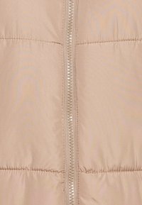 Veste doudoune beige clair avec une texture lisse et brillante. Présente une fermeture éclair centrale et des sections matelassées horizontales pour l'isolation.