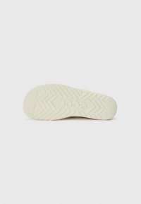 Cremefarvet sneakersål med zigzag mønster, rund form og tekstureret overflade. Logo og mærkenavn synligt.