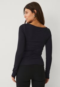 Zwarte top met lange mouwen en een ronde hals, zachte textuur en geplooide details aan de achterkant, gecombineerd met zwarte leggings.