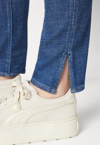 Blå denimjeans med en liten splitt i kanten, paret med off-white suedestøvler med en teksturert overflate og merkevaredetaljer.