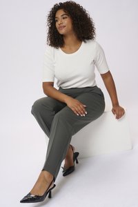 Top bianco a maniche corte, pantaloni olive verdi su misura e décolleté nere con punta a slingback e un accento decorativo. Tessuto liscio e design aderente.