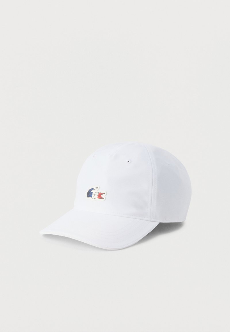 Λευκό καπέλο μπέιζμπολ με κυρτό γείσο και μικρό κεντητό λογότυπο κροκοδείλου σε κόκκινο, άσπρο και μπλε στο κέντρο του μπροστινού μέρους.