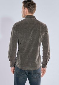 Schmal geschnittenes, langärmliges Shirt aus dunkelgrünem Cordstoff mit abgerundetem Saum, Knopfmanschetten und spitzem Kragen. Dezente Textur von oben bis unten.