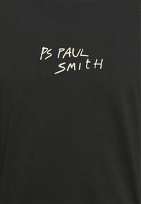 Musta kangas, jossa valkoisella käsinkirjoitustyylillä teksti "PS PAUL SMITH" keskittyneenä rinta-alueelle.