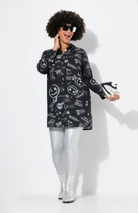 Vestido negro de camisa con impresiones gráficas blancas; combinado con leggings plateados brillantes y botines metálicos; sosteniendo un clutch plateado.
