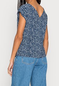 Top blu navy con un motivo astratto bianco, maniche corte e scollatura a V sul retro, abbinato a jeans ampi in denim blu chiaro.