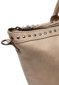 Beige faux läder handväska med nitar och dragkedja på toppen. Har en strukturerad yta och runda handtag för enkel bärning.