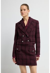 Veste en tweed bordeaux à double boutonnage, motif écossais et boutons décoratifs, associée à une jupe assortie.