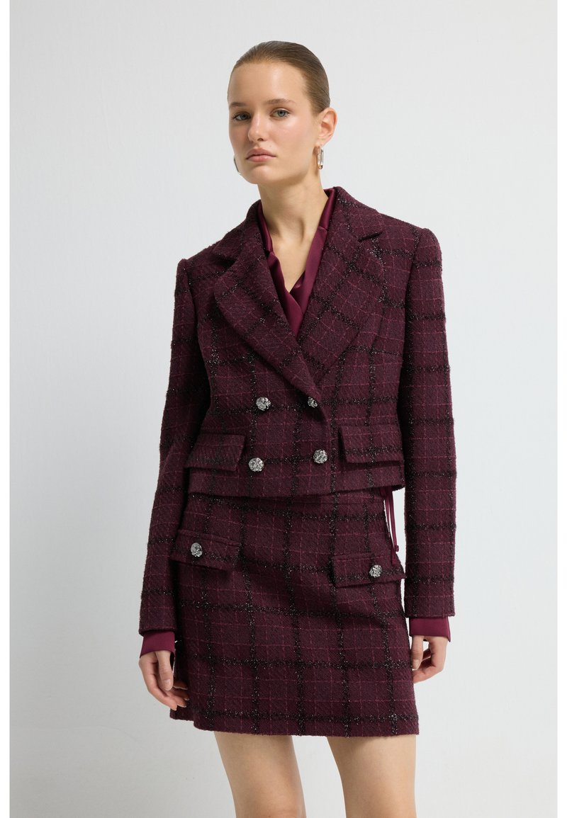 Veste en tweed bordeaux à double boutonnage, motif écossais et boutons décoratifs, associée à une jupe assortie.