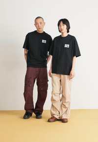 Black cotton t-shirts with graphic logos, paired with brown cargo pants featuring multiple pockets and cream wide-leg trousers.