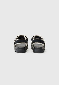 Black and white crocheted sandals with chunky black soles, viewed from the back on a plain light background.