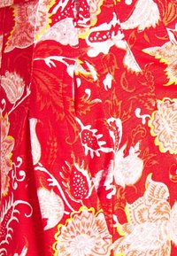 Tessuto rosso con un motivo floreale in bianco e giallo, caratterizzato da disegni intricati di fiori e foglie. Materiale morbido e testurizzato con caduta.