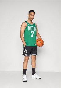 Maillot de basket vert avec l'inscription "BOSTON" et le numéro "7", short noir avec des accents blancs, baskets blanches, tenant un ballon de basket orange.
