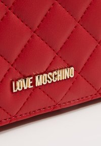 Červená prošívaná kožená taška s zlatým logem "LOVE MOSCHINO". Povrch má hladkou texturu s jasně patrnými diamantovými vzory.