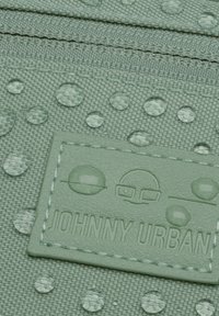 Green fabric wallet featuring raised water droplets, textured surface, and a stitched logo patch labeled “JOHNNY URBAN.”