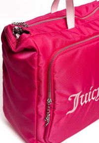 Rosane Nylon-Tasche mit zwei Reißverschlüssen, ausgestattet mit einem Reißverschluss-Zipper in Silberoptik und gesticktem "Juicy"-Logo. Glatte Textur und strukturierte Form.