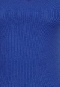 Ribbad, åtsittande topp i starkblått tyg. Slät yta med vertikala linjer. Enkel halsringning, inga ytterligare dekorationer eller mönster.