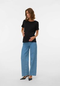 Camiseta de maternidad negra de manga corta combinada con jeans de pierna ancha de color azul claro y tacones negros con lunares; textura de algodón suave, diseño sencillo.